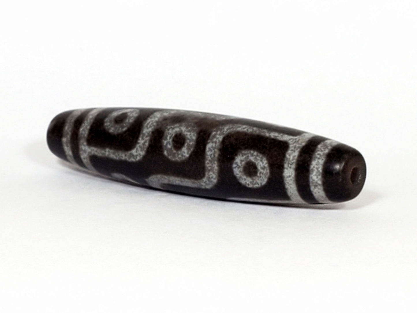 N-062226-9E, angled view toward narrow tapered tip, drill hole centred, nine eye motif wrapping body, unretouched