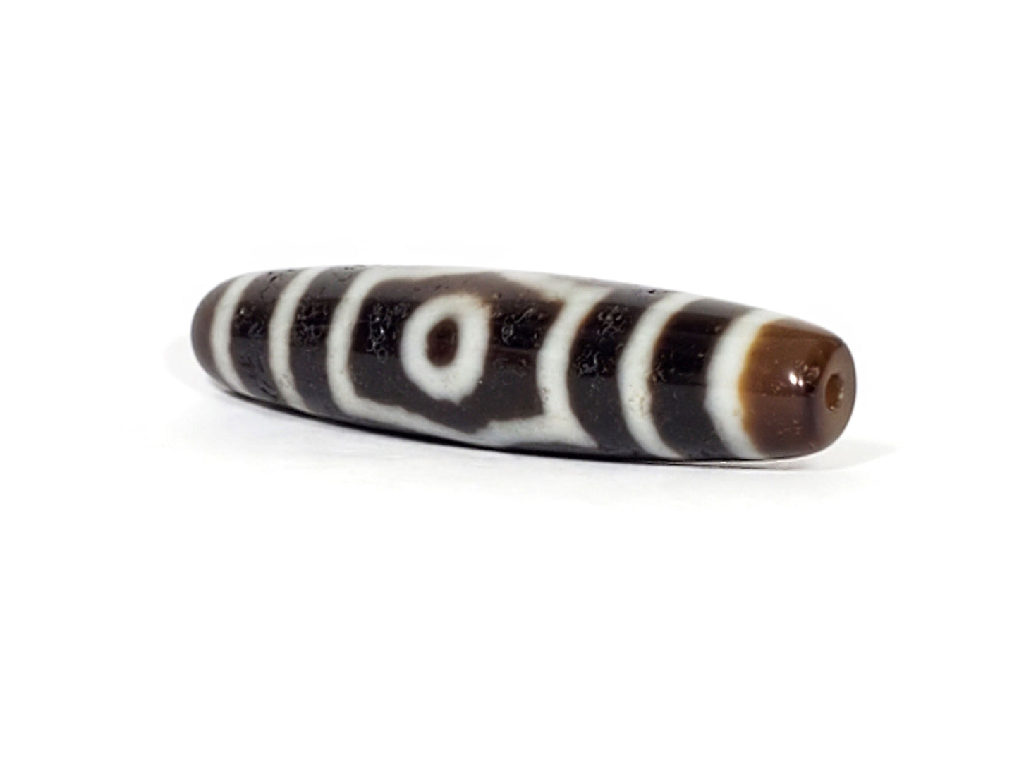 V-070226-ThE-001 dzi bead, diagonal view showing drill hole, warm brown end zone, unretouched photo.
