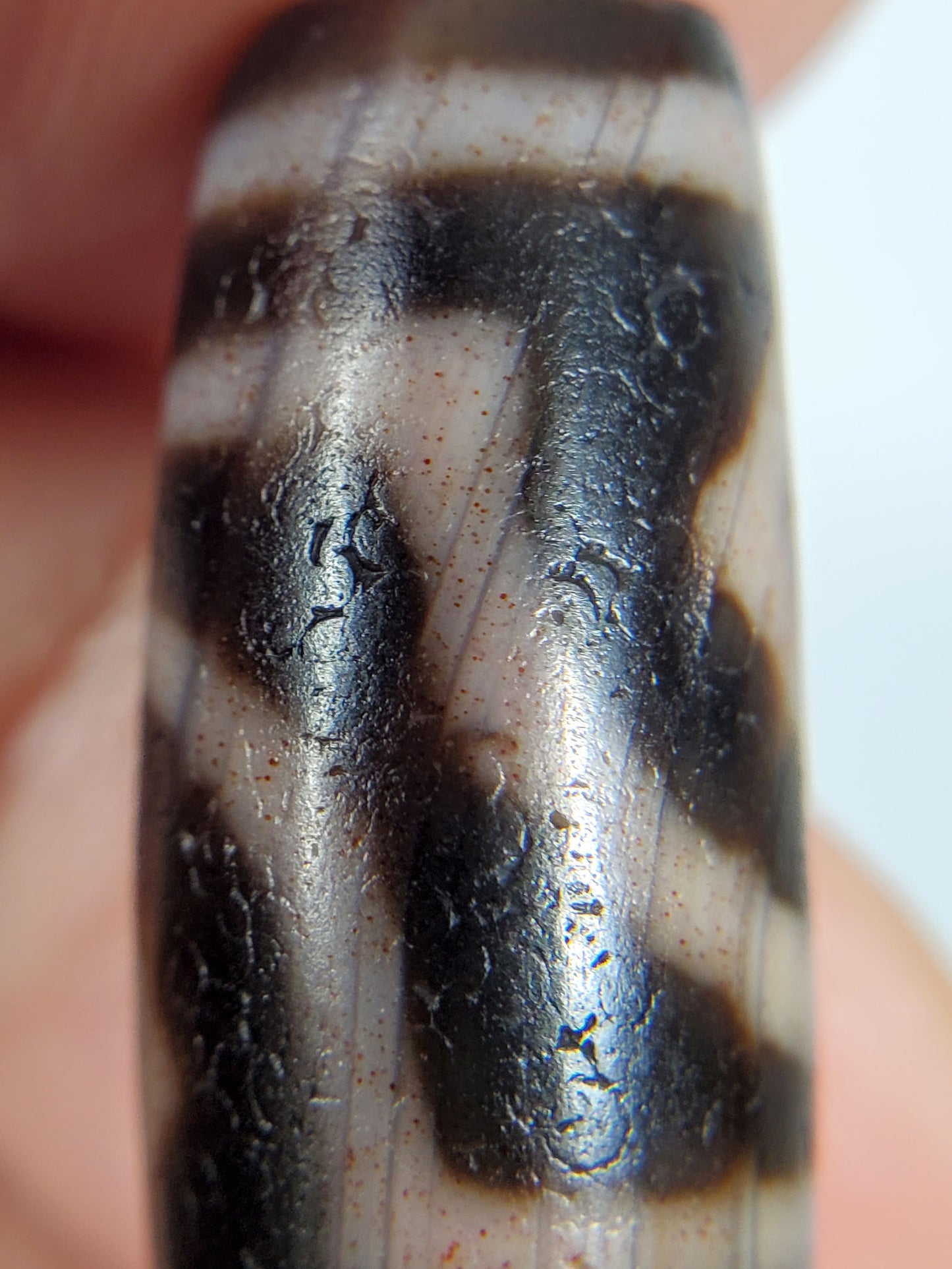 Macro: ancient dzi tip zone — black ground with crackle pitting and red-orange bloodspot dots, Anc-0426-2DE