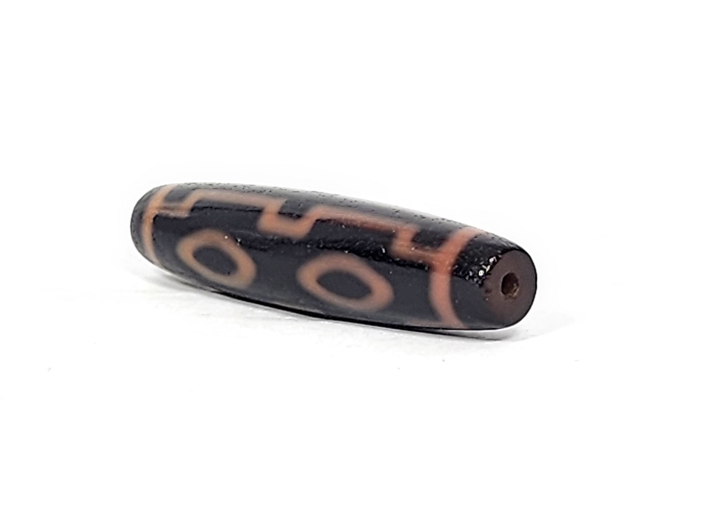 Three-quarter view of antique Four Eye dzi At-012325-4E, dark brown end cap with drill hole, amber motif lines wrapping torpedo body, 51.9mm × 12.2mm, unretouched