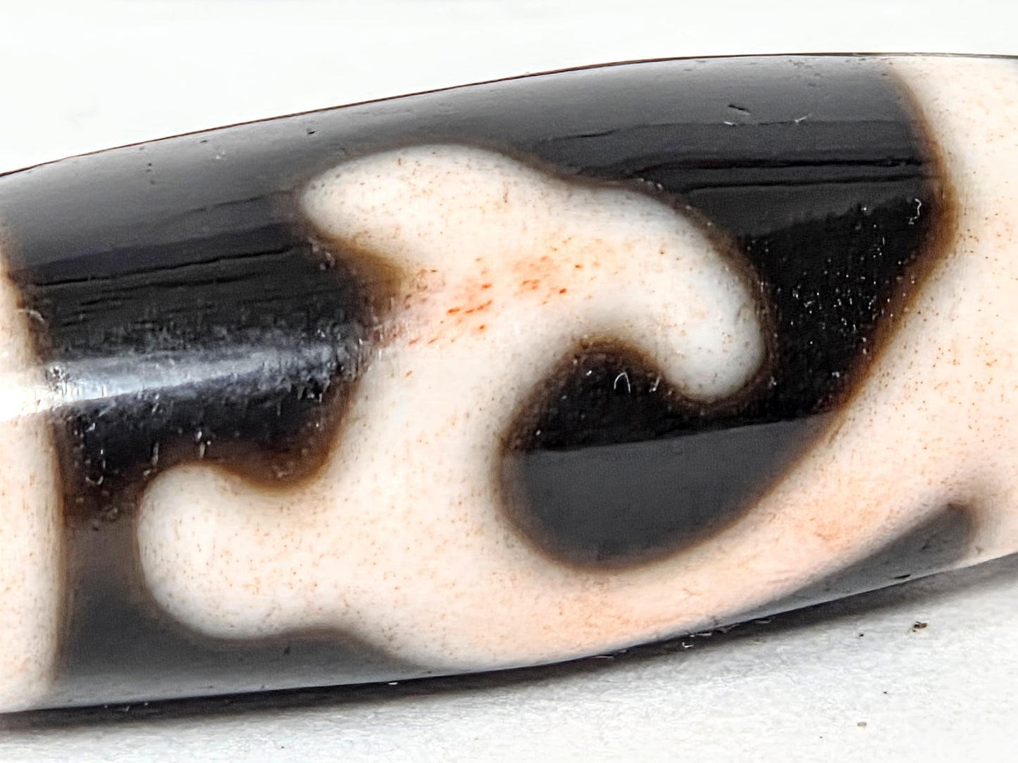 Macro close-up of antique Tibetan Green Tara Dzi bead focal piece showing Tara motif, natural cinnabar bloodspot specks and amber striations — unretouched photo — Ancient Dzi Shop
