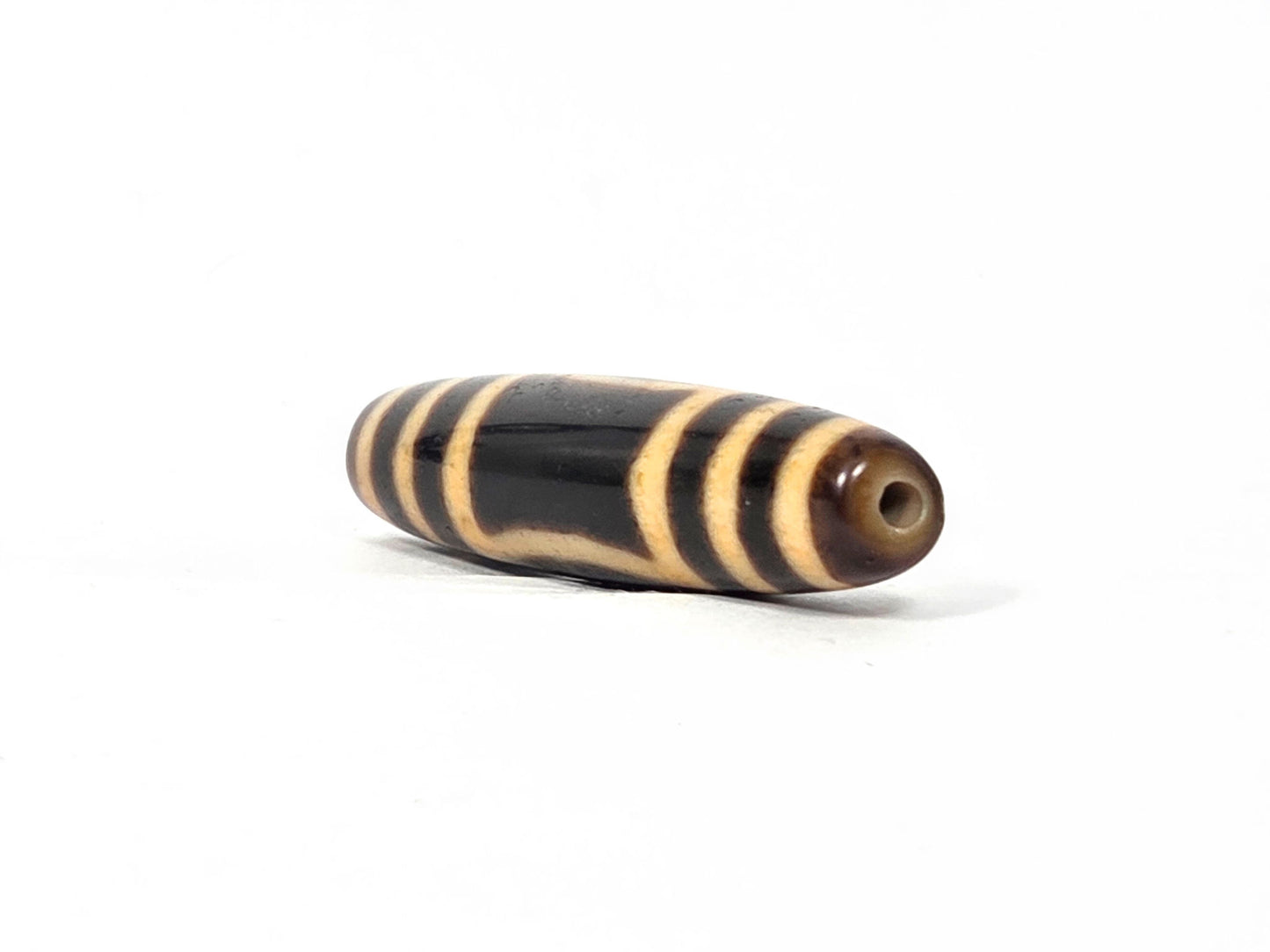 Antique heaven earth dzi — opposite end, drill hole at warm brown tip, amber concentric rings on black body, At-0426-HE