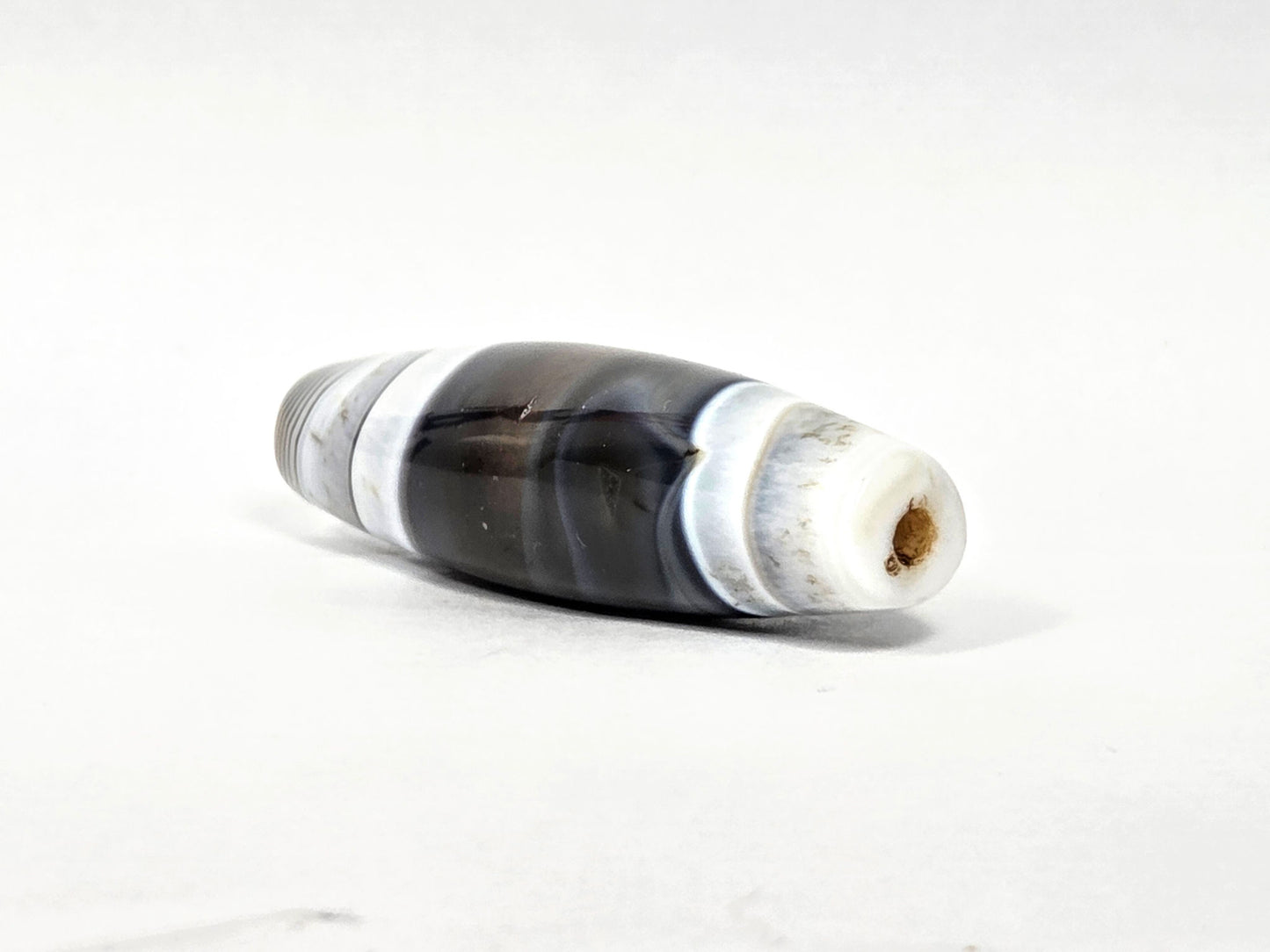 At-N-071426-NBA end angle A — wider end cap, concentric micro-banding, brown drill channel patina, unretouched.
