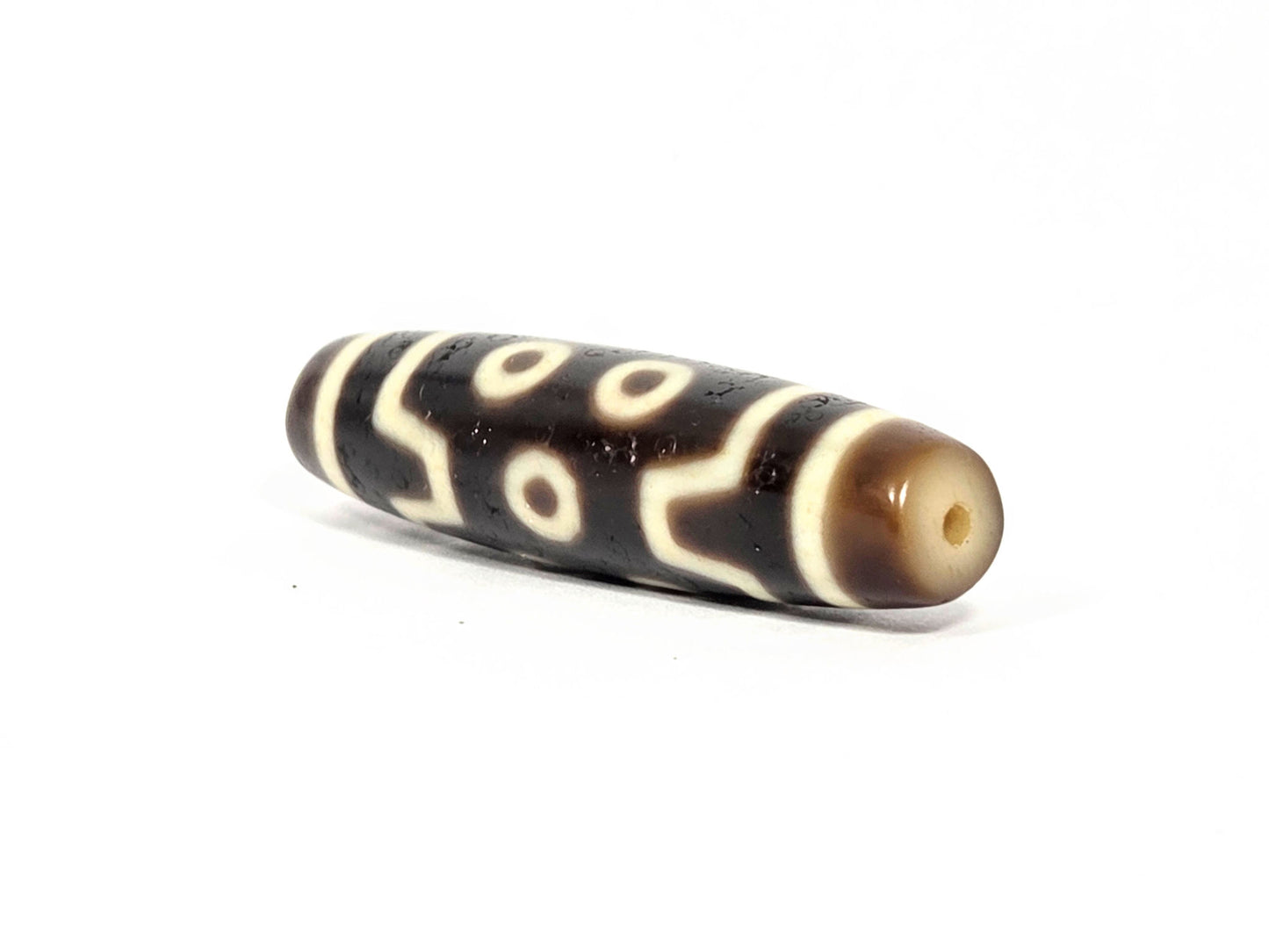 At-072226-7E end angle A — cream-beige end cap, small tan drill opening, S-curve motif wrap visible, unretouched.