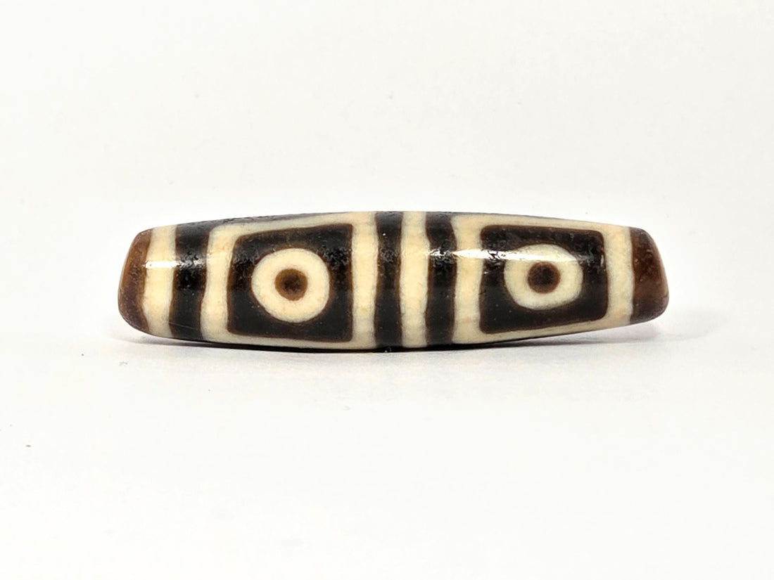 Ancient Tibetan four-eye dzi bead — genuine dark brown and cream agate with four bold eye motifs, showing natural surface patina and original etching consistent with extreme age