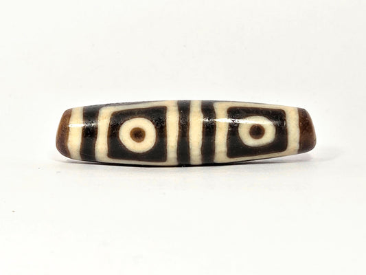 Ancient Tibetan four-eye dzi bead — genuine dark brown and cream agate with four bold eye motifs, showing natural surface patina and original etching consistent with extreme age