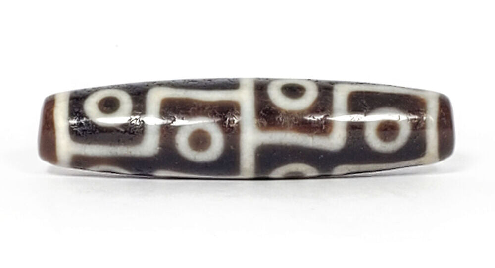 Ancient Tibetan twelve-eye dzi bead — warm dark brown agate with bold cream white etched eye motifs densely arranged across the surface, showing natural patina and surface weathering consistent with extreme age, unretouched photo by Ancient Dzi Shop