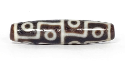 Ancient Tibetan twelve-eye dzi bead — warm dark brown agate with bold cream white etched eye motifs densely arranged across the surface, showing natural patina and surface weathering consistent with extreme age, unretouched photo by Ancient Dzi Shop