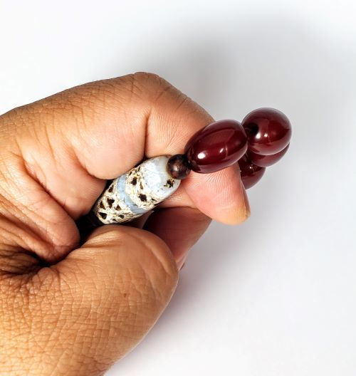 Authentic ancient Tibetan dzi bead held in hand alongside deep red Faturan mala beads — Ancient Dzi Shop unretouched