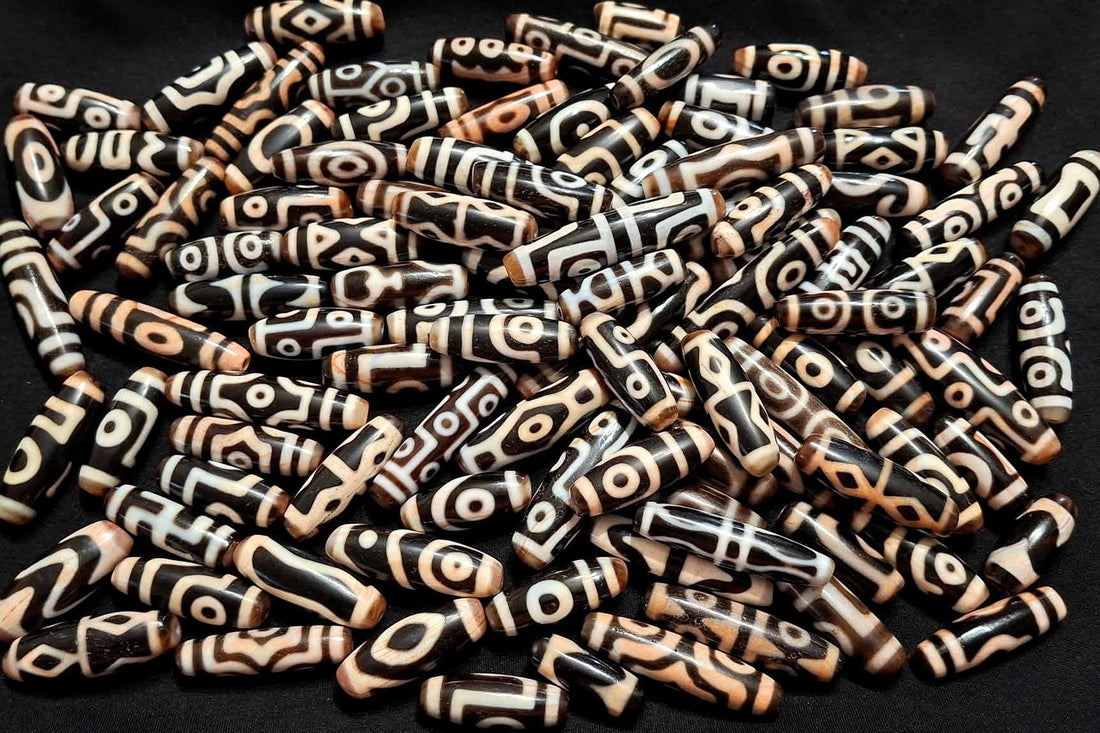 Authentic Tibetan dzi beads displaying various motifs including eye patterns, lotus, tiger tooth, vajra, and other sacred Buddhist symbols