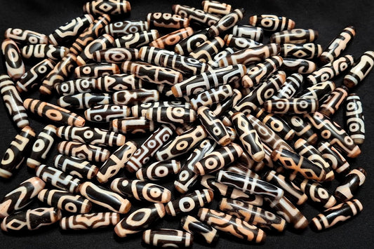 Authentic Tibetan dzi beads displaying various motifs including eye patterns, lotus, tiger tooth, vajra, and other sacred Buddhist symbols