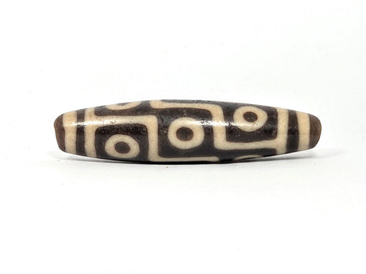 Original authentic ancient Tibetan nine-eye dzi bead — cream and dark brown agate with nine bold eye motifs, heavy surface patina consistent with extreme age, unretouched photo by Ancient Dzi Shop