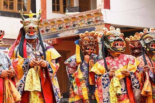 Tibetan monks performing Cham dance in monastery courtyard — masked ritual dance of Vajrayana Buddhism