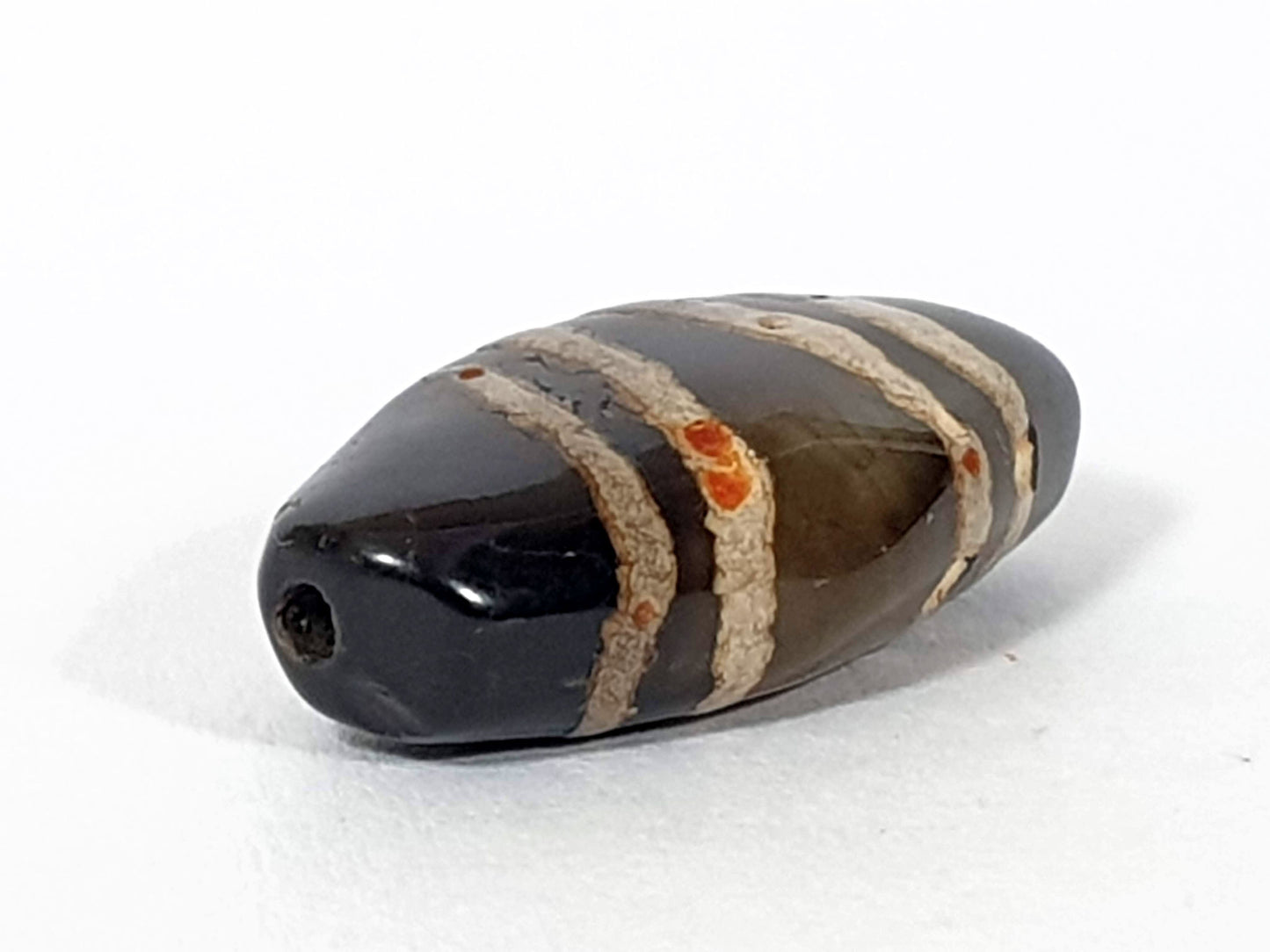 Ac-111720-7SOS, left end 3/4 view, pitch-black tip, drill hole, cinnabar bloodspot clusters in beige stripes, unretouched