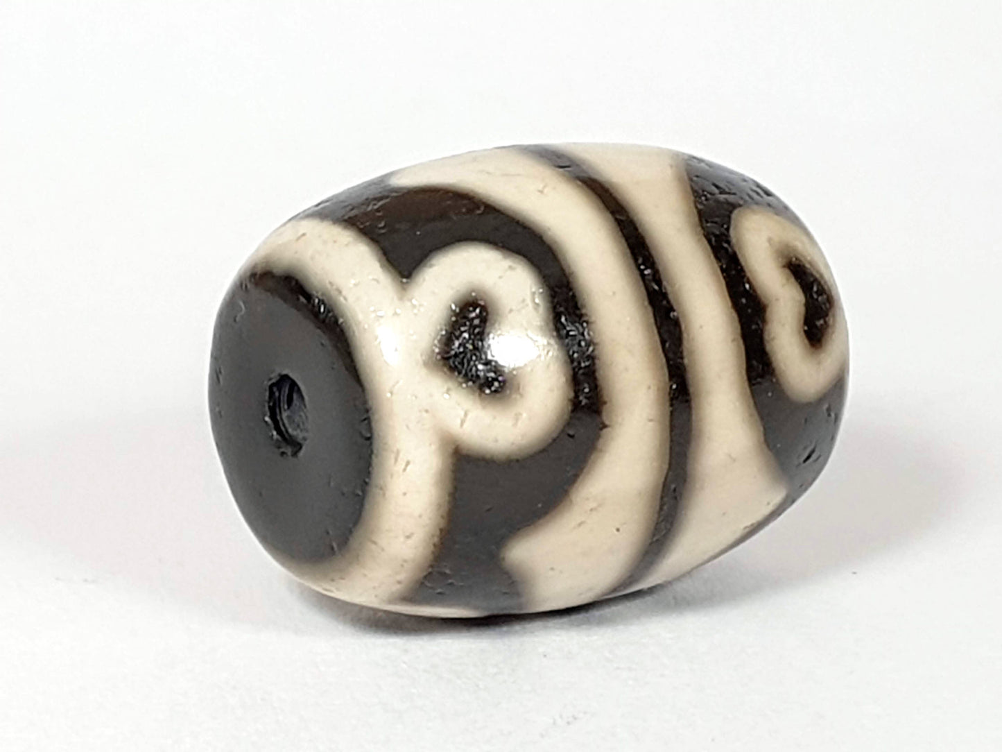 N-062226-TTSEL, reverse side view, flowing dark brown motif lines on cream-ground barrel, drill hole visible, unretouched