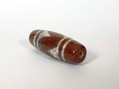 N-062426-TTBS Bead A tiger tooth dzi angled view warm reddish-brown ground sandy-cream tooth motif drill hole unretouched