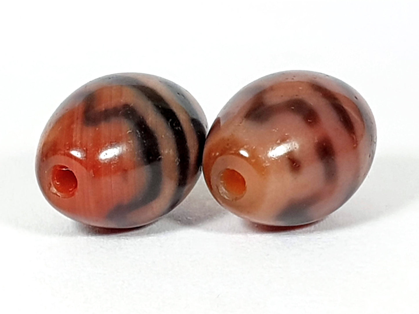 At-062926-TTBS pair drill-end view, warm orange-red channel visible both beads, tiger tooth banding, agate, unretouched