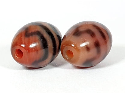 At-062926-TTBS pair drill-end view, warm orange-red channel visible both beads, tiger tooth banding, agate, unretouched