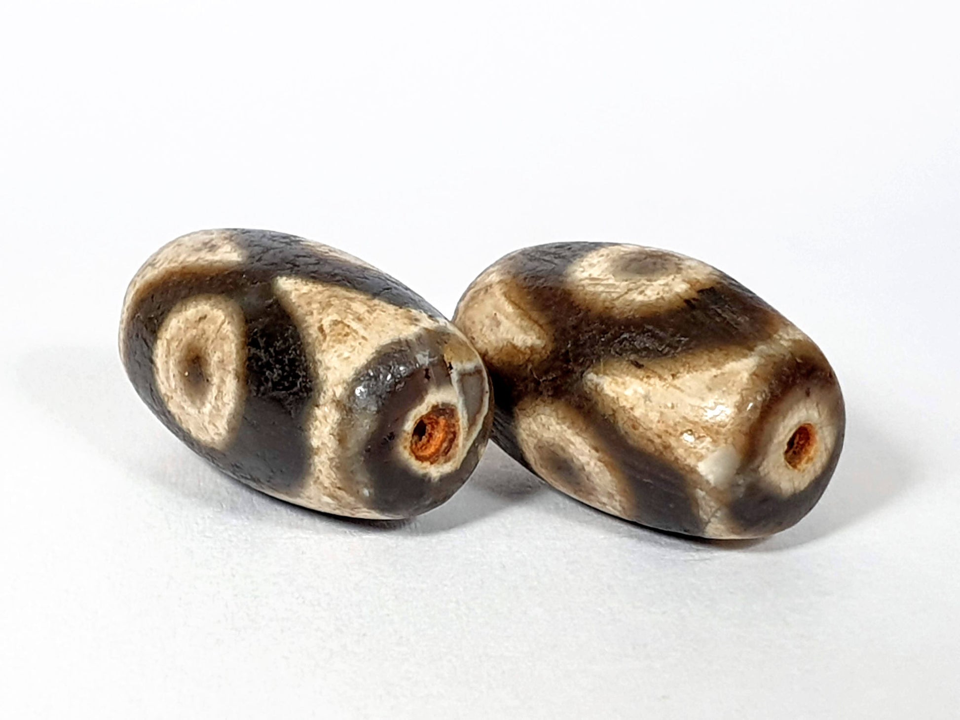 N-FA-062626-3E pair three eye dzi, angled view, drill ends, rust-orange interiors visible, cream sandy ground, unretouched