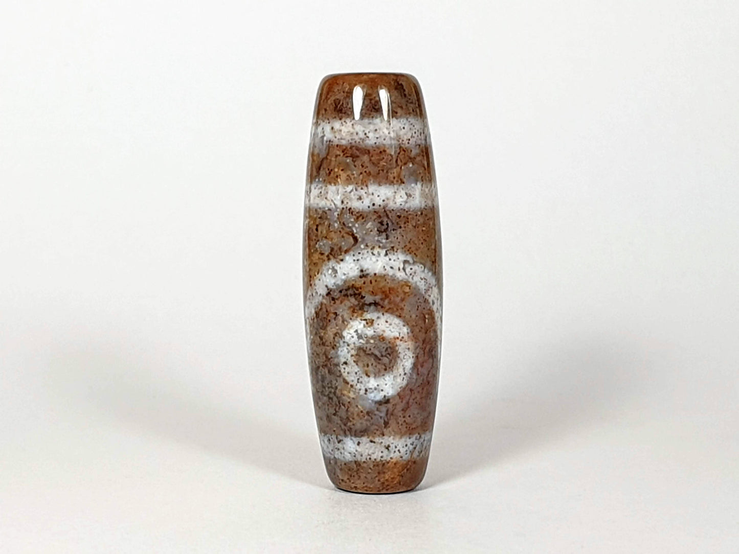 N-062126-2E dzi bead, standing end view showing drill hole detail, unretouched