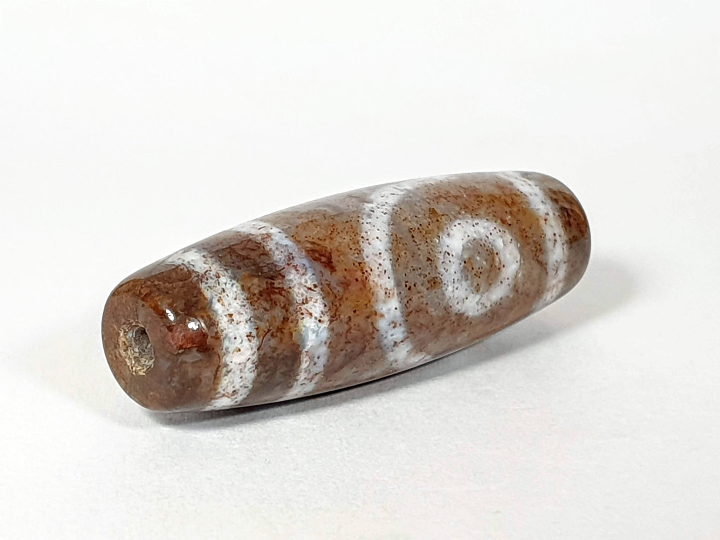 N-062126-2E dzi bead, angled view of drilled end with mineral deposit, unretouched