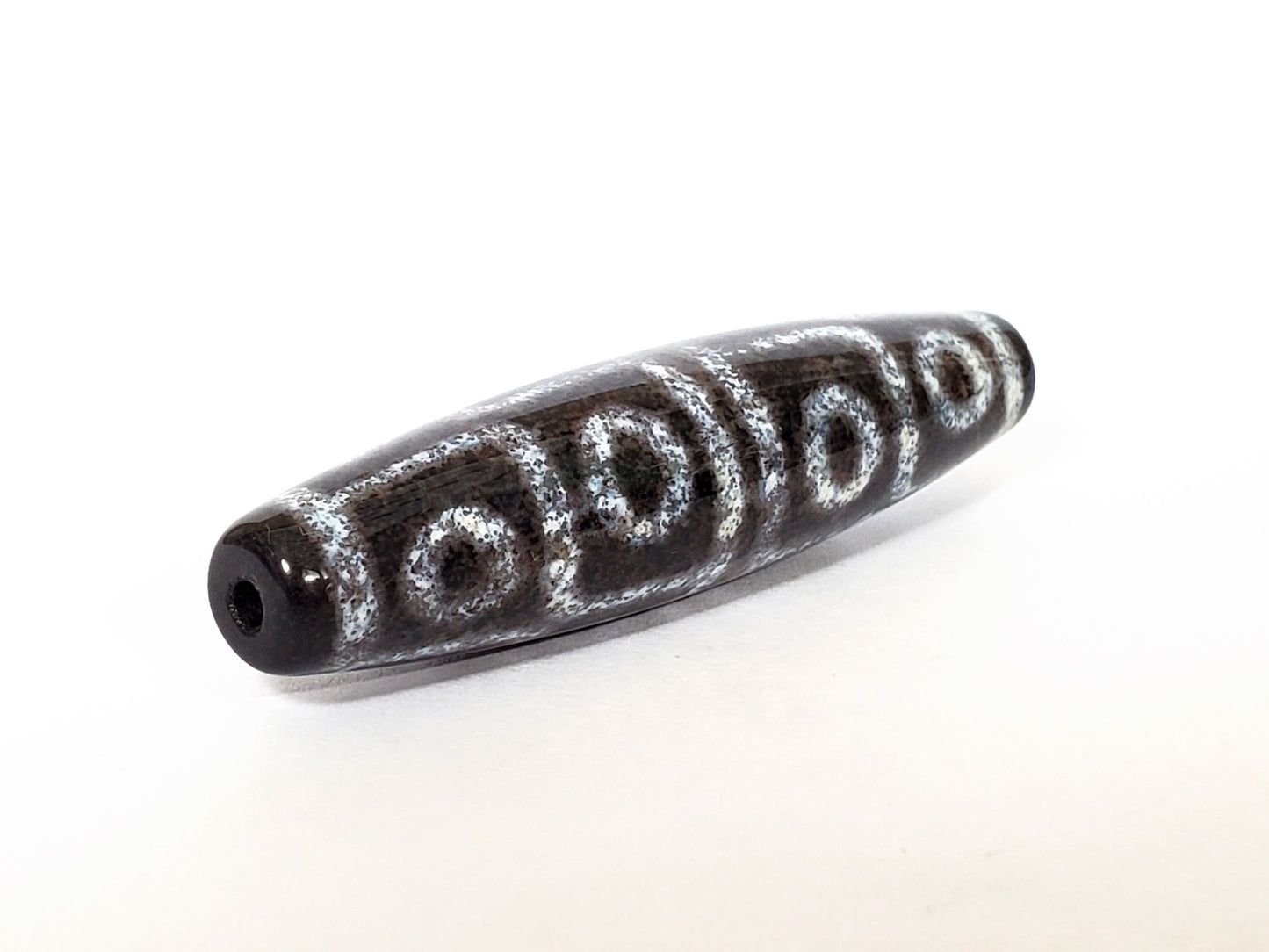 N-062126-12E-2 dzi bead, three-quarter angle showing drilled end, unretouched