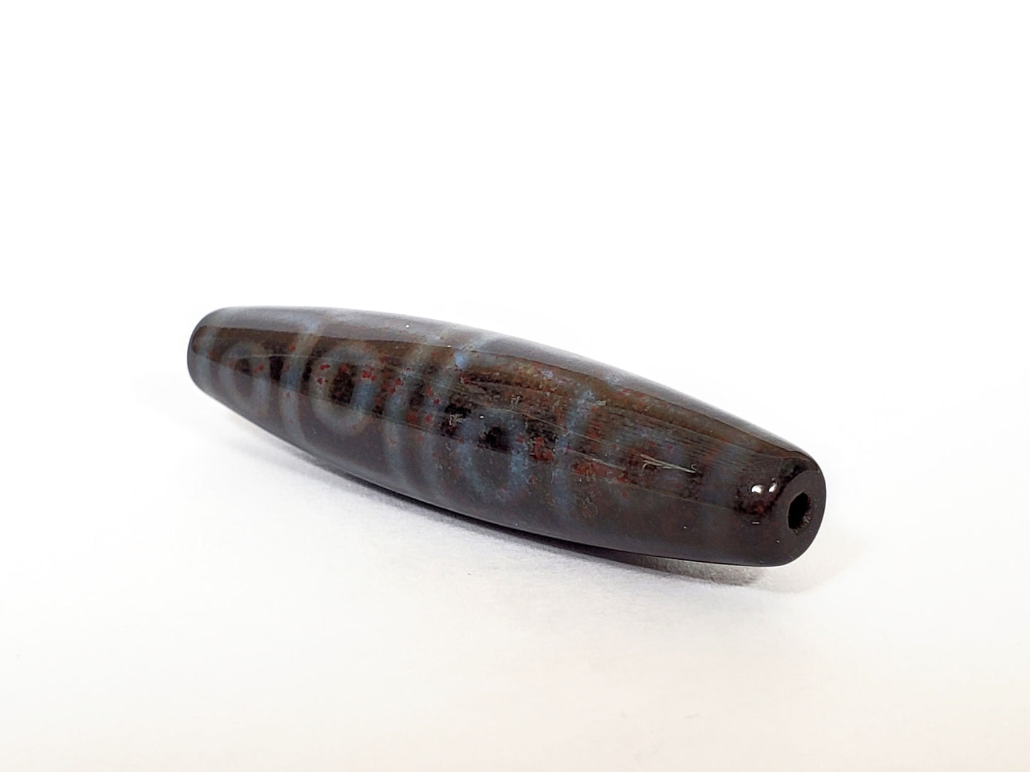 N-062126-12E-1 dzi bead, three-quarter angle showing drilled end, unretouched