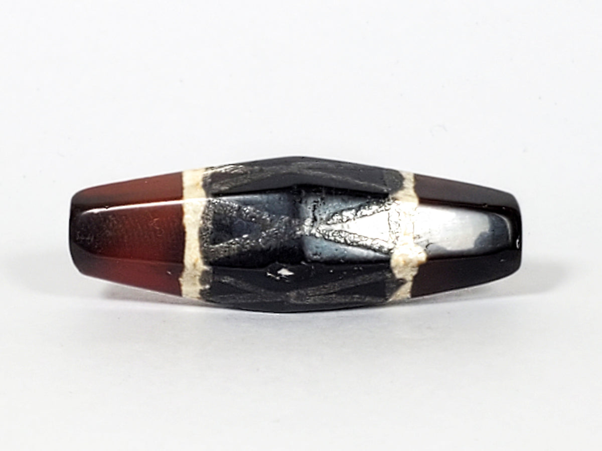 Ancient hexagonal carnelian dzi bead, black criss-cross motif, cream white bands, worn patina, visible drill hole, deep red agate body