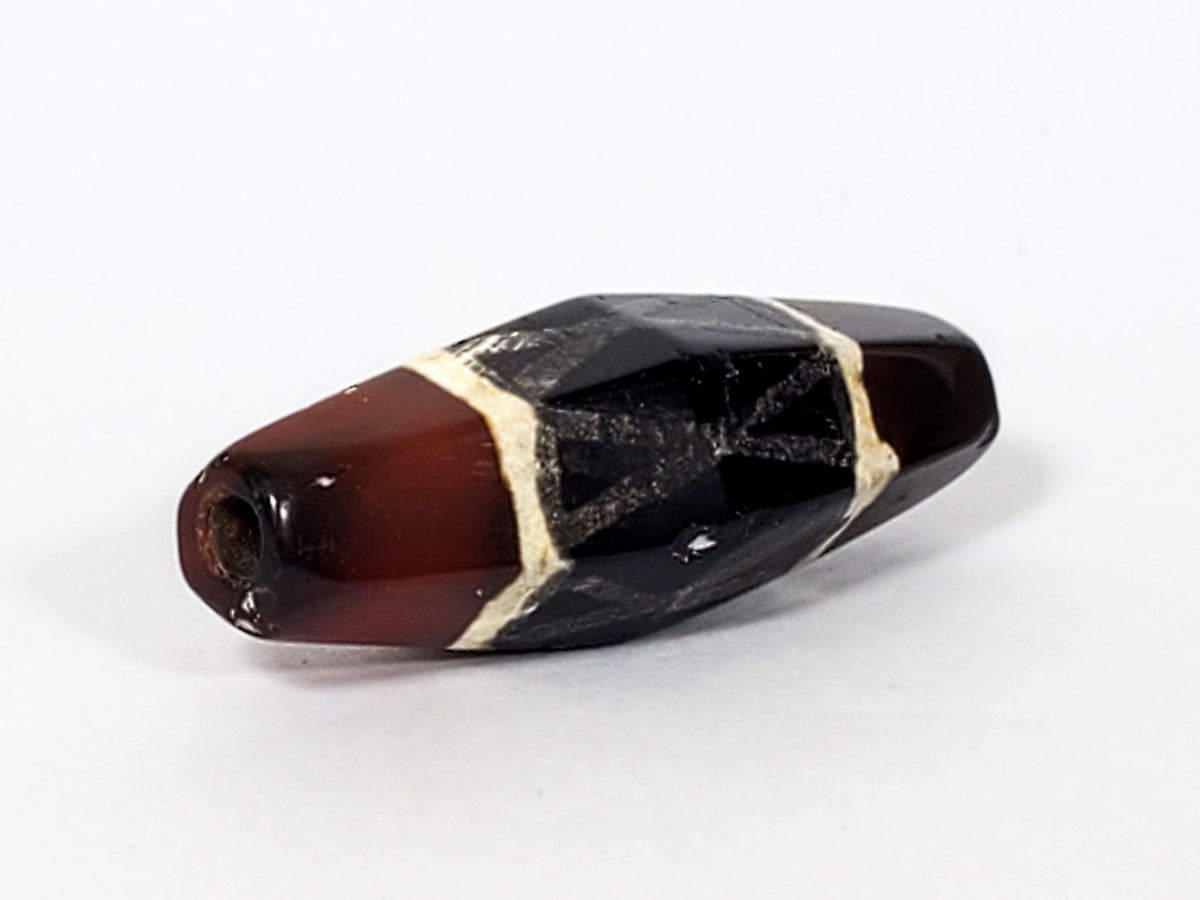 Ancient carnelian dzi bead, hexagonal shape, black criss-cross motif, cream lines, deep red agate, visible drill hole, aged patina
