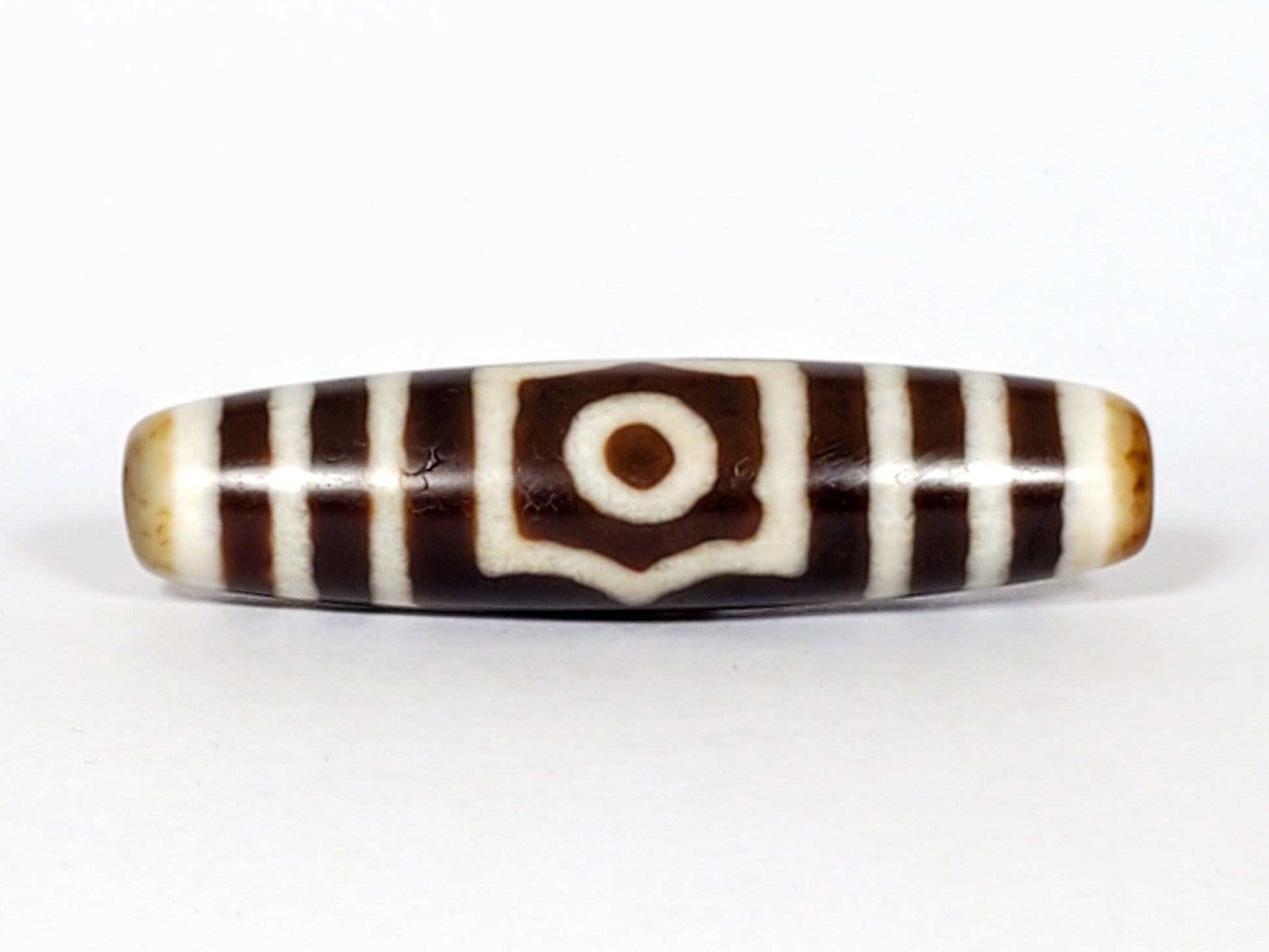 Antique three eye dzi At-053126-3E, Face A, single concentric-ring eye in octagonal cream frame, warm brown agate, honey-tan end caps, 51.2mm × 13.0mm, unretouched