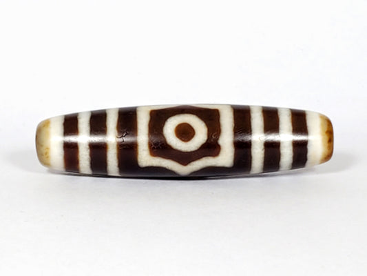 Antique three eye dzi At-053126-3E, Face A, single concentric-ring eye in octagonal cream frame, warm brown agate, honey-tan end caps, 51.2mm × 13.0mm, unretouched