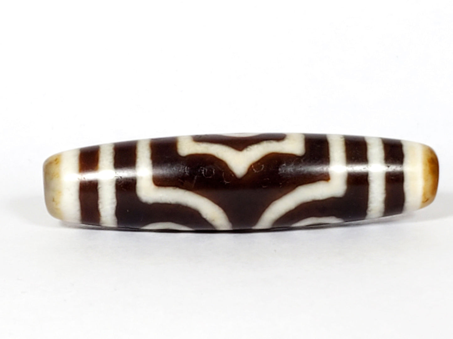 Face B of antique three eye dzi At-053126-3E, double arch crown motif in cream on warm brown agate, no eye on this face, honey-tan end caps, 51.2mm, unretouched photography