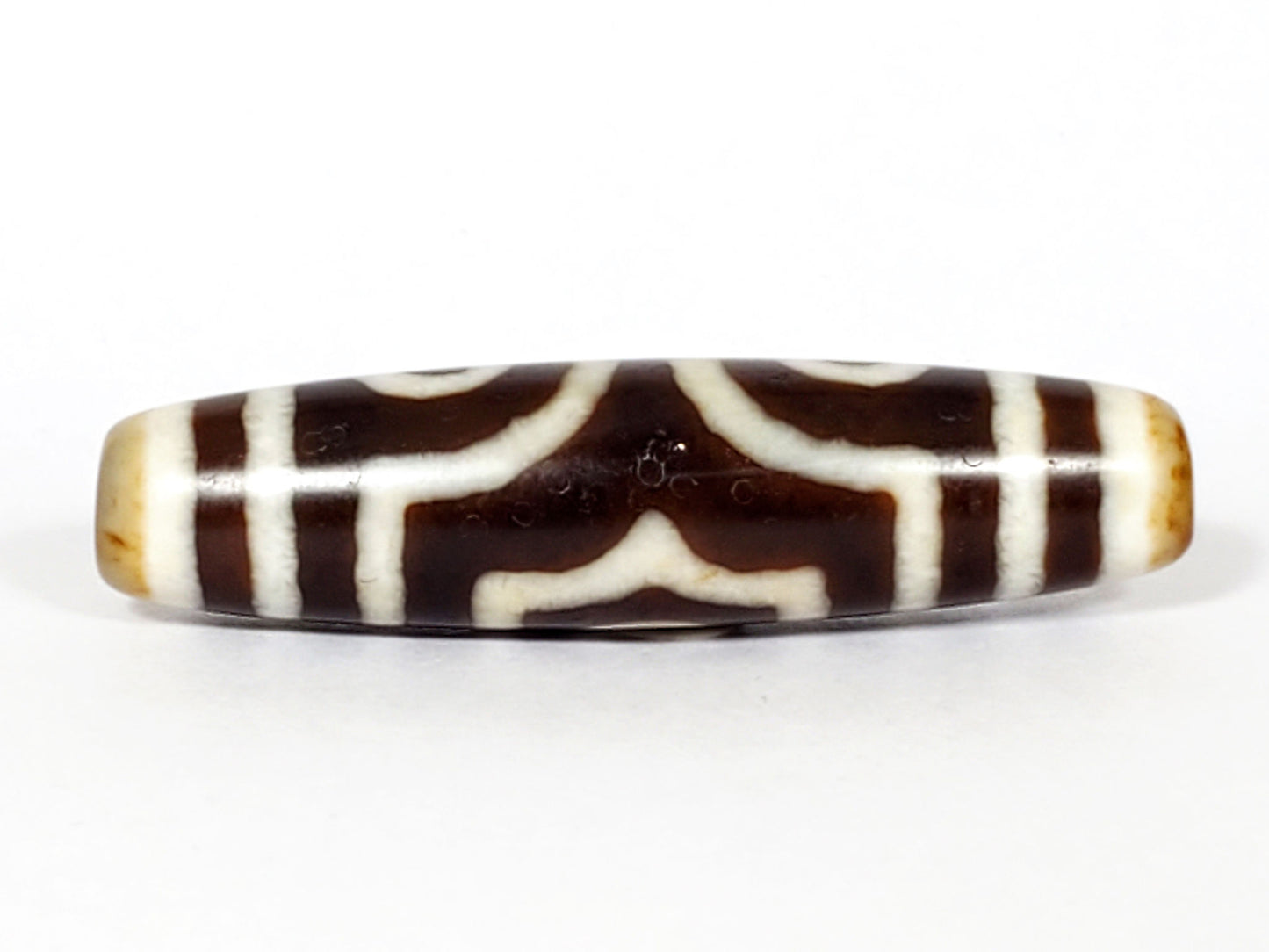 Face D of antique three eye dzi At-053126-3E, arch crown motif reversed as chevron forms on warm brown agate, structural cream lines, honey-tan end caps, unretouched