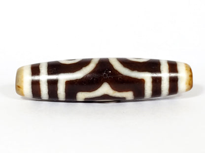 Face D of antique three eye dzi At-053126-3E, arch crown motif reversed as chevron forms on warm brown agate, structural cream lines, honey-tan end caps, unretouched