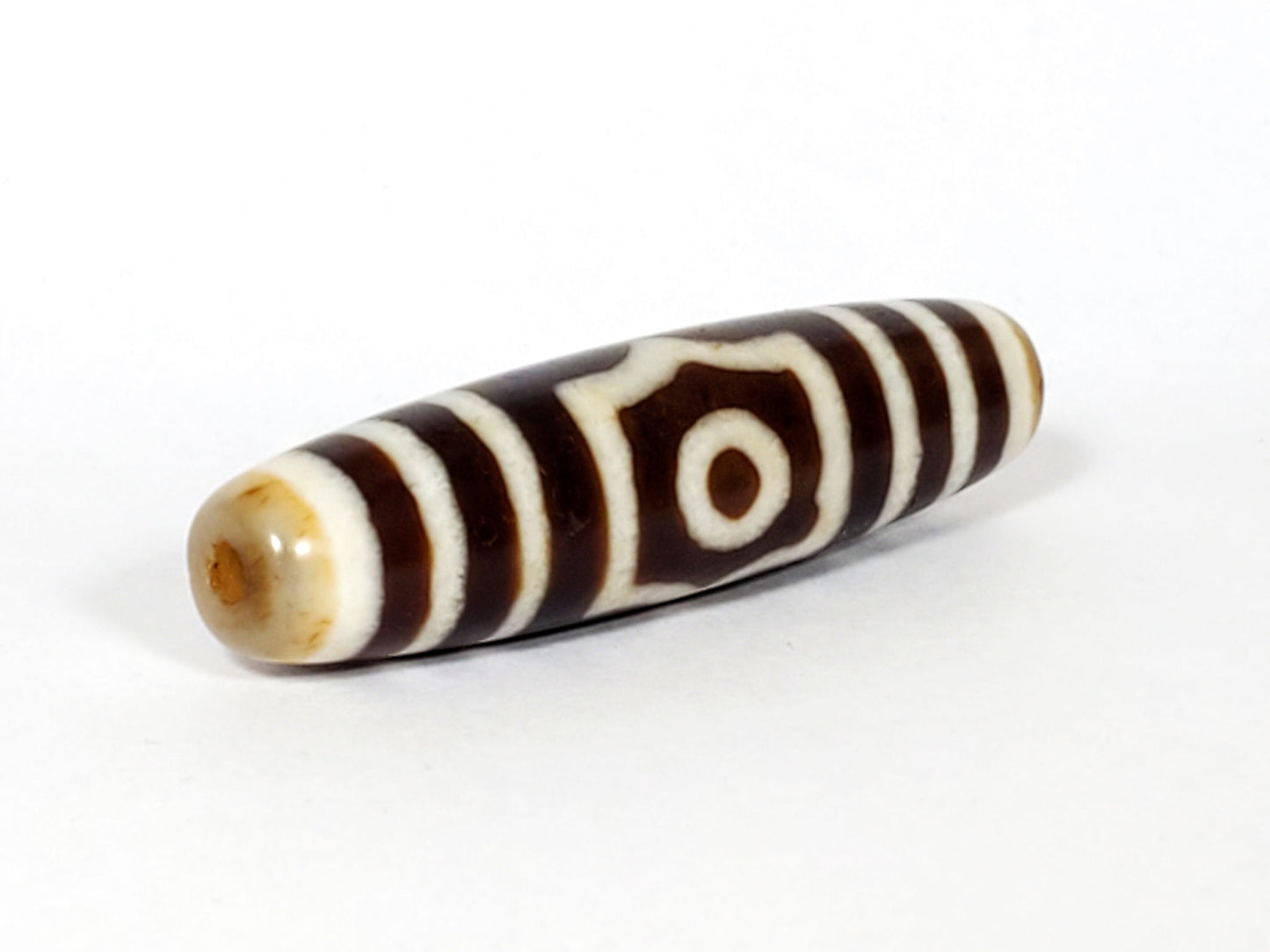 Opposite end cap of antique three eye dzi At-053126-3E, warm honey-tan agate tip with drill hole, single-eye frame face visible, elongated torpedo 51.2mm, unretouched photography