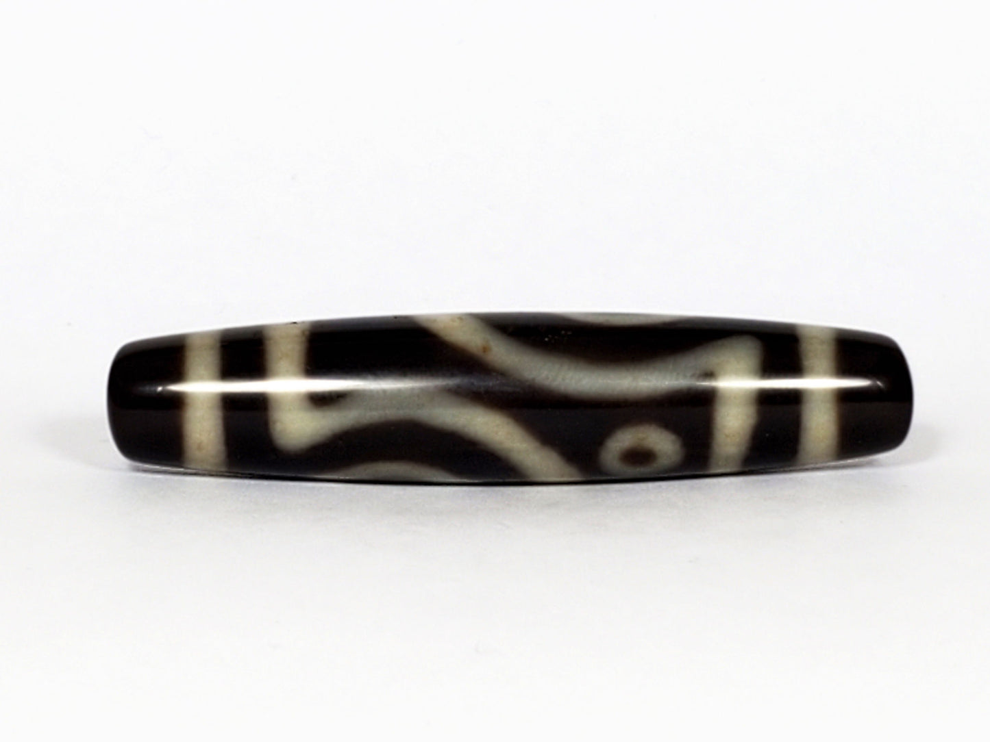 V-070226-4E2 dzi bead, angled view, curved cream lines on black ground, unretouched.