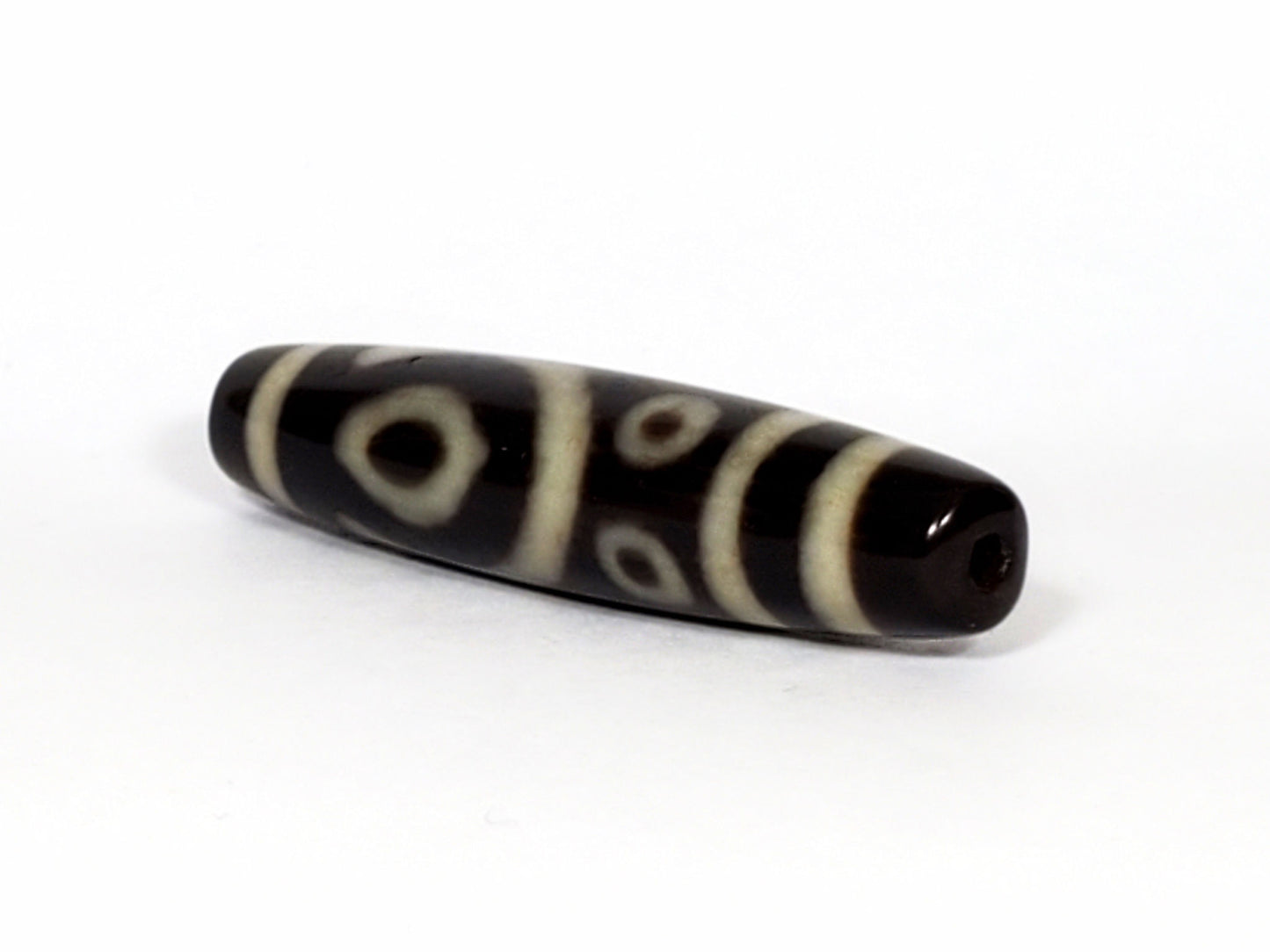 V-070226-4E2 dzi bead, diagonal view showing drill hole, black ground, unretouched photo.