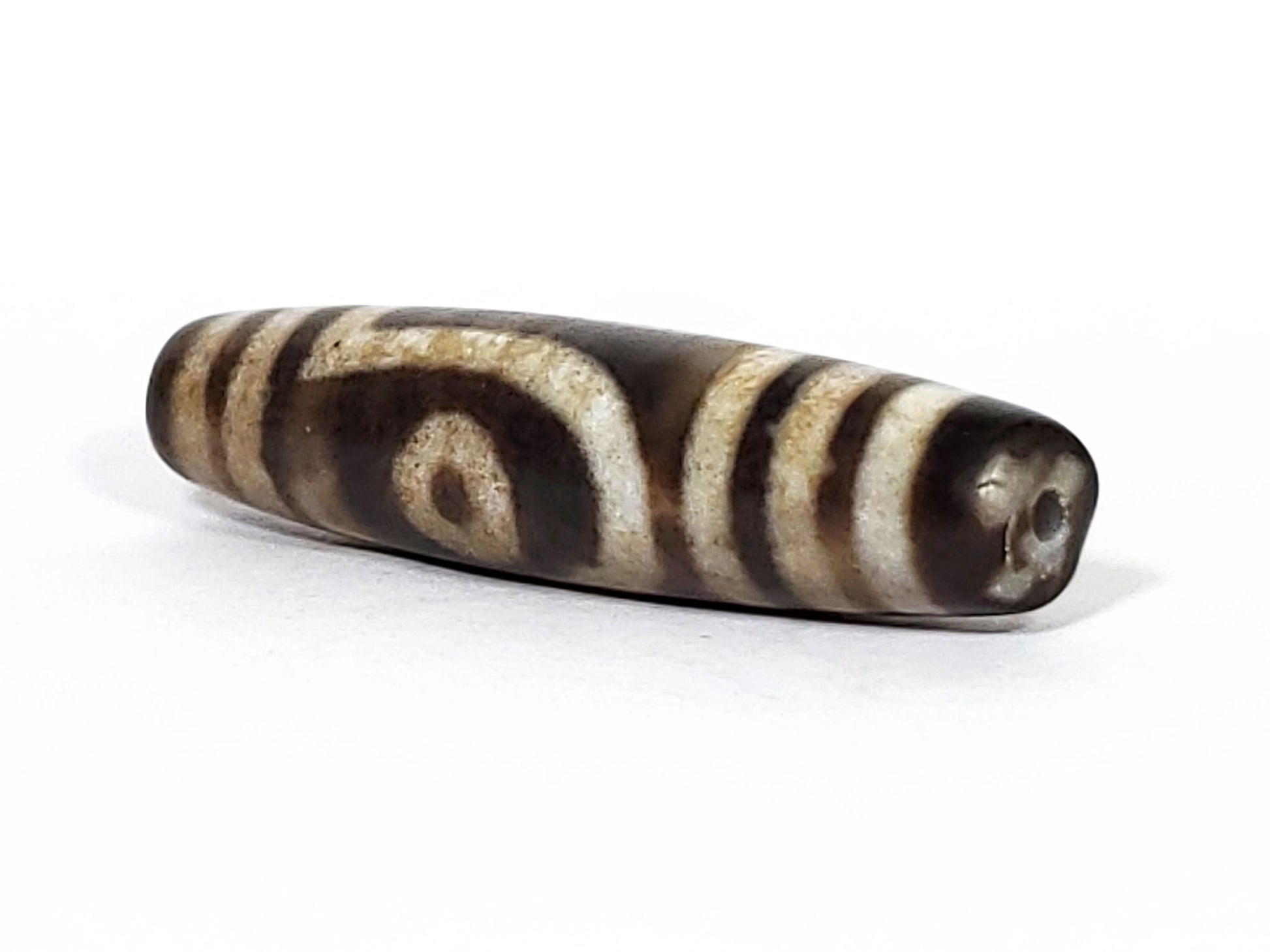 N-062126-2E2 dzi bead, angled view showing dark tapered tip and drill hole, unretouched