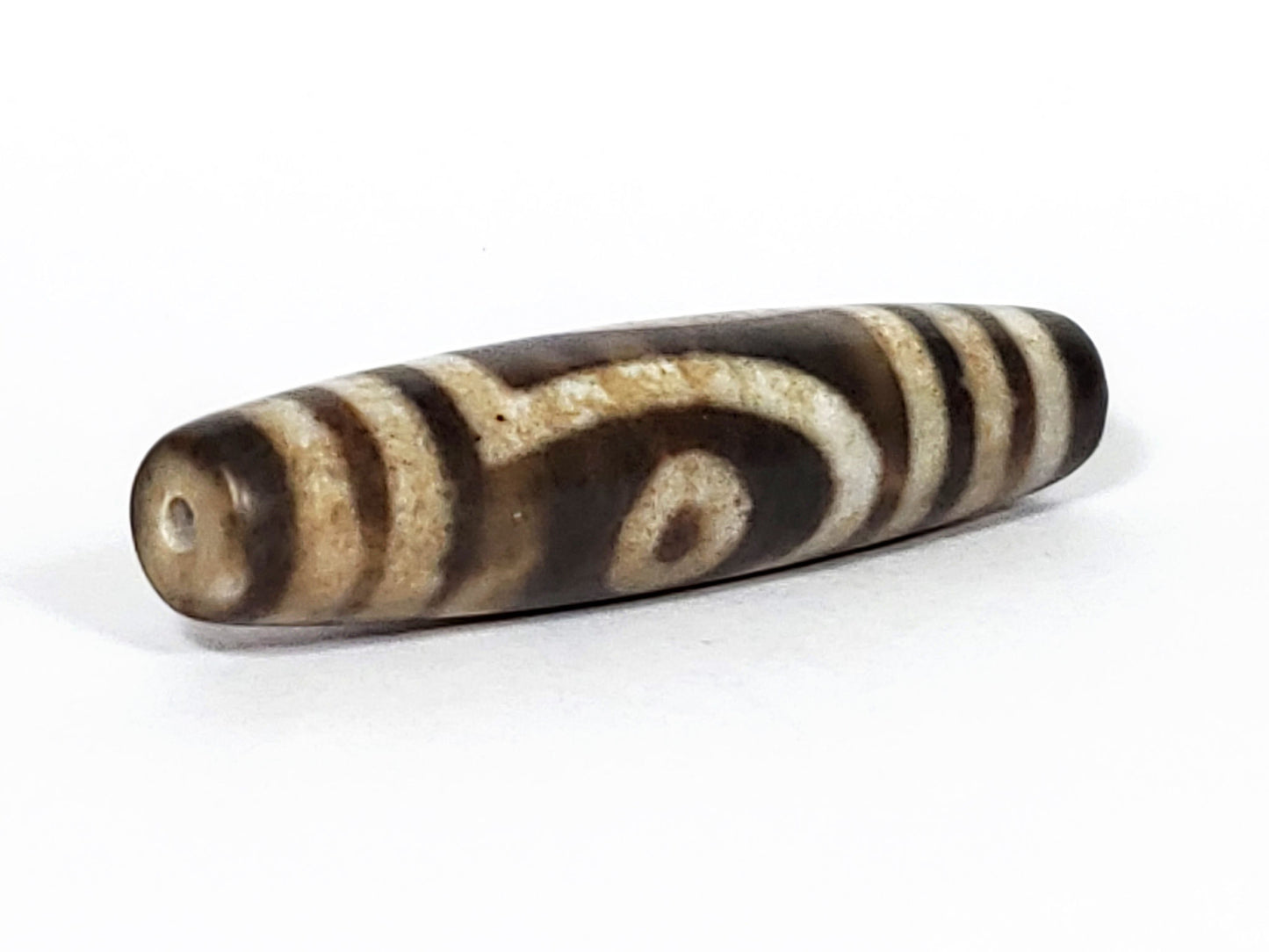 N-062126-2E2 dzi bead, opposite angled view, dark tip and drill hole, unretouched