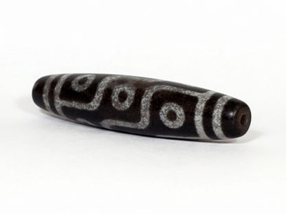 N-062226-9E, angled view toward narrow tapered tip, drill hole centred, nine eye motif wrapping body, unretouched
