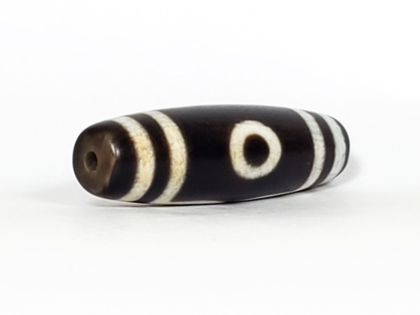 N-070226-3E dzi bead, diagonal view showing drill hole, black ground, unretouched photo.