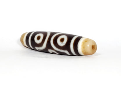 Opposite end cap of antique six eye dzi At-053026-6E, warm honey-gold agate tip with drill hole, open-ring eye pair visible, full 54.9mm torpedo body, unretouched photography