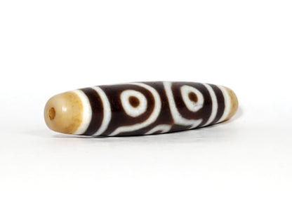 Three-quarter view of antique six eye dzi At-053026-6E, honey-gold end cap with drill hole, two closed eyes visible, elongated torpedo body, deep brown agate, 54.9mm, unretouched