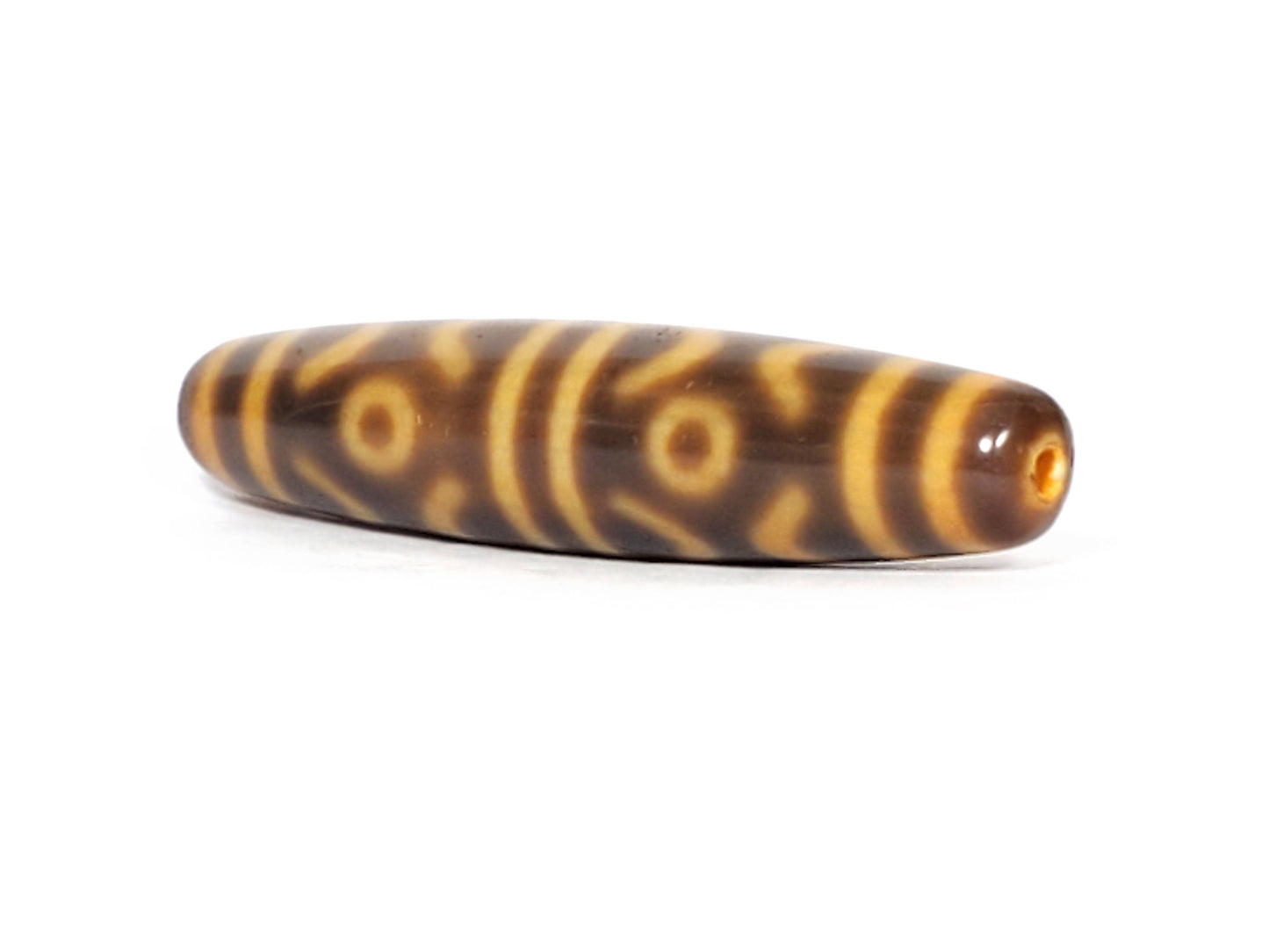 At-053126-6ETT, angled view showing honey-gold end cap and drilled hole, six eye tiger tooth motif, unretouched