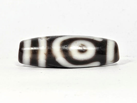 Antique Tibetan two eye dzi bead At-010726-2E3, front face, bold closed concentric-ring eye on near-black agate, vertical stripes right, 38.6mm × 12.5mm, unretouched