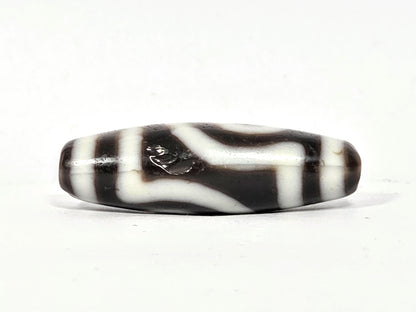 Side profile of antique two eye dzi bead At-010726-2E3, torpedo body, near-black agate, cream vertical stripes, medicine digs visible, 38.6mm × 12.5mm