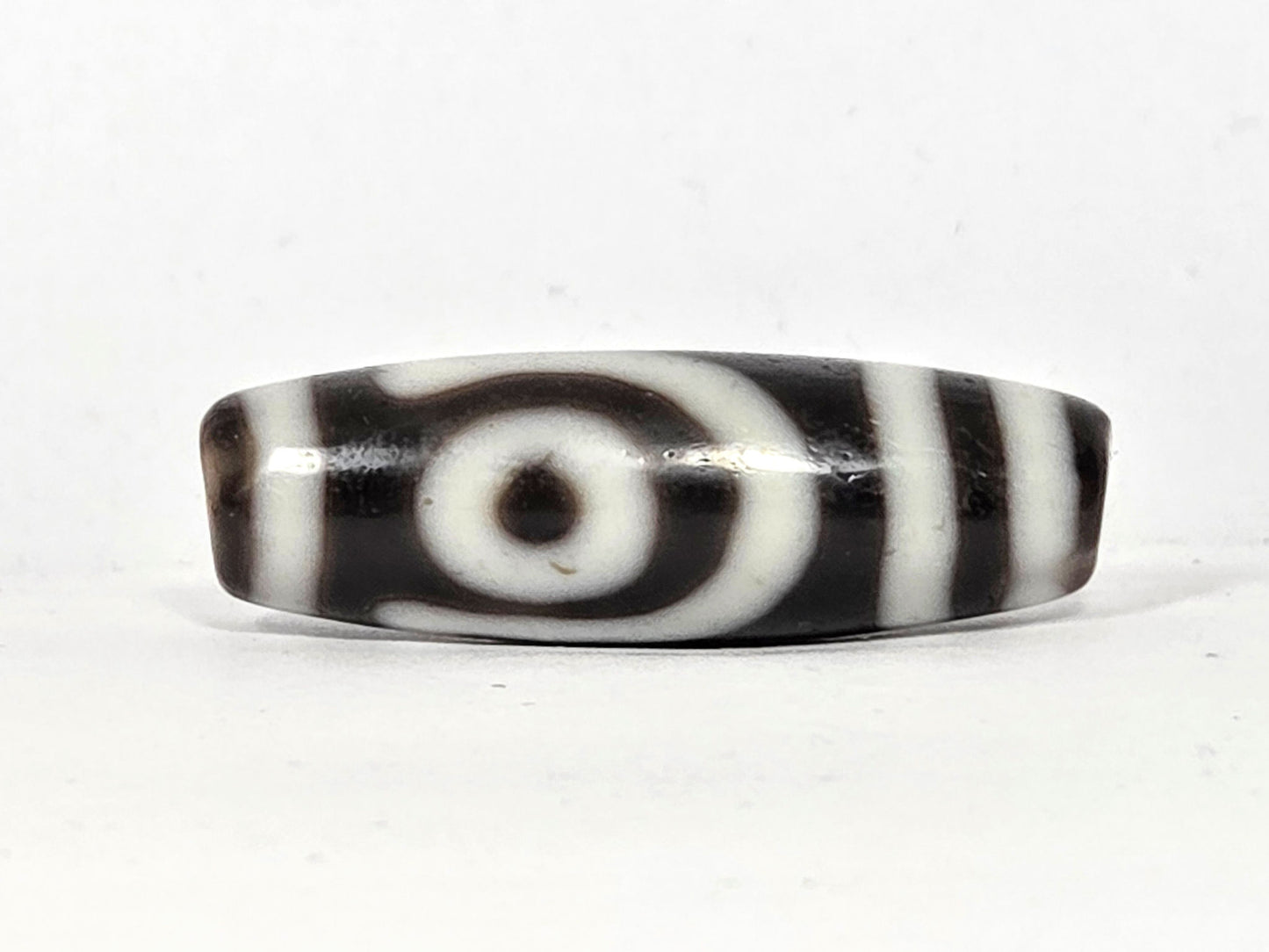 Second eye face of antique two eye dzi bead At-010726-2E3, closed concentric-ring eye with dark pupil on near-black agate, flanked by vertical stripes, unretouched