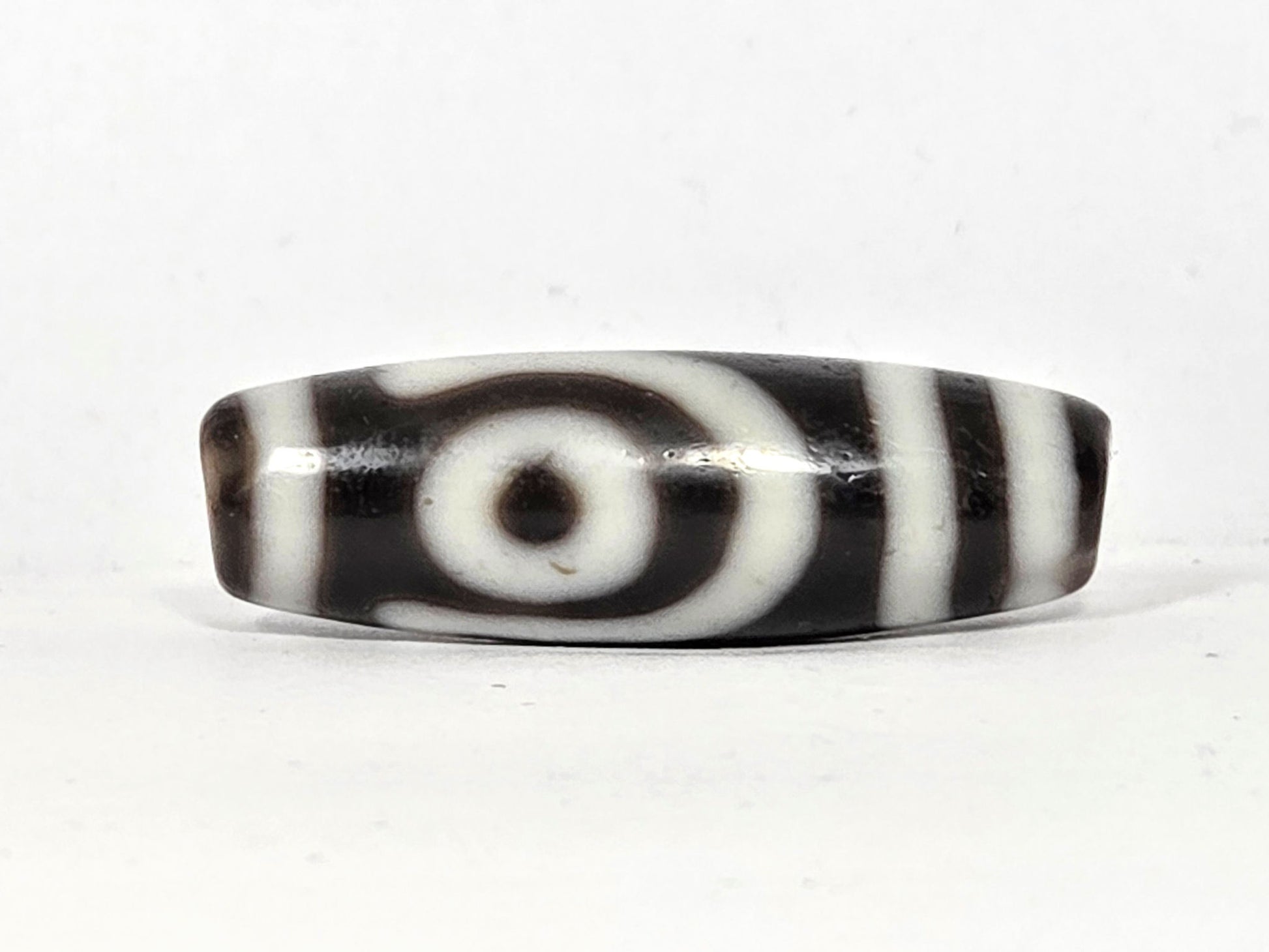 Second eye face of antique two eye dzi bead At-010726-2E3, closed concentric-ring eye with dark pupil on near-black agate, flanked by vertical stripes, unretouched