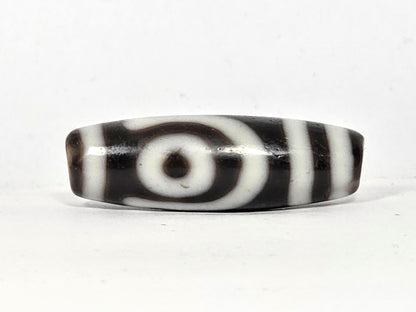 Second eye face of antique two eye dzi bead At-010726-2E3, closed concentric-ring eye with dark pupil on near-black agate, flanked by vertical stripes, unretouched