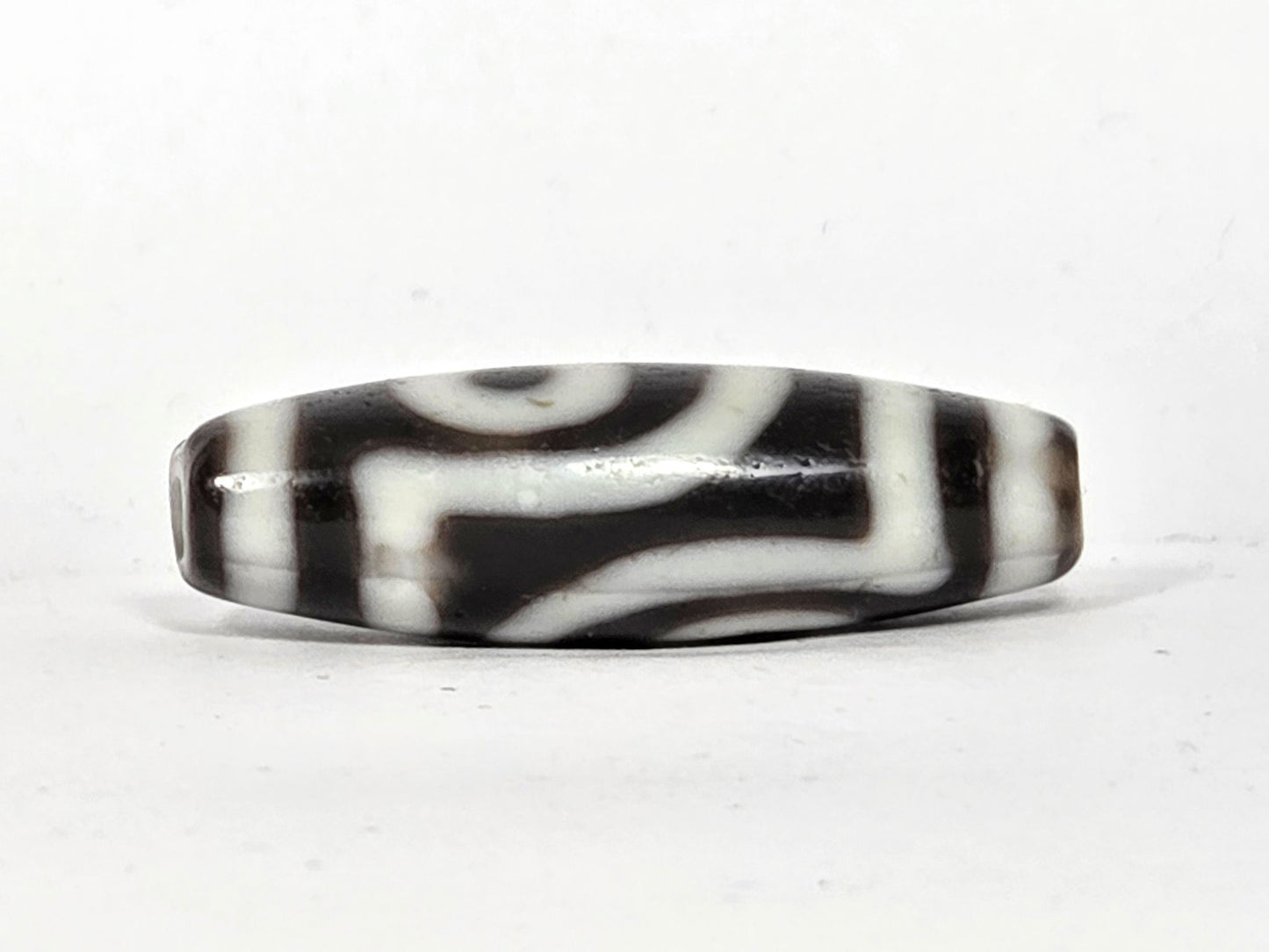 Angled view of antique two eye dzi bead At-010726-2E3 showing body profile, dark brown end cap, near-black agate torpedo form, 38.6mm × 12.5mm